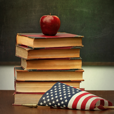 A stack of books with an apple placed on top and an American flag placed in front